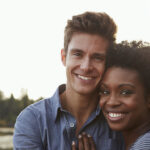 A mixed race couple smiles as they embrace outside