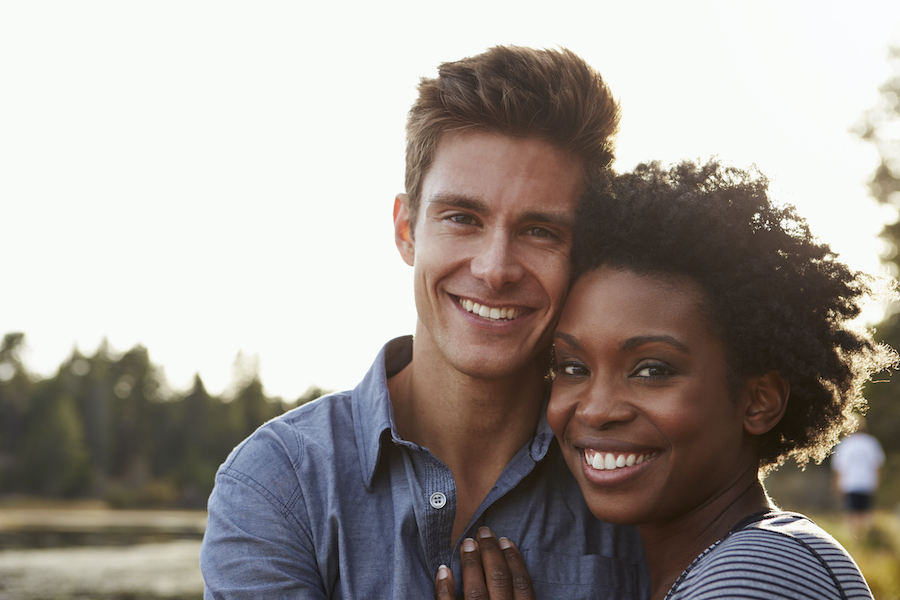 A mixed race couple smiles as they embrace outside