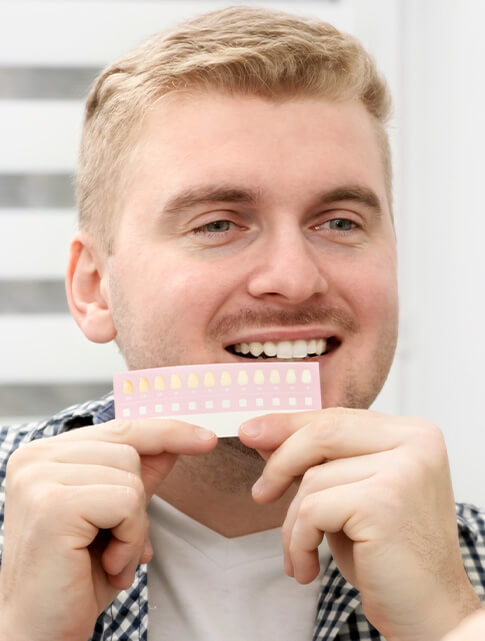 man comparing teeth to whitening chart