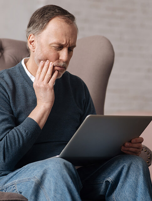 man holding his jaw in pain while looking at his laptop