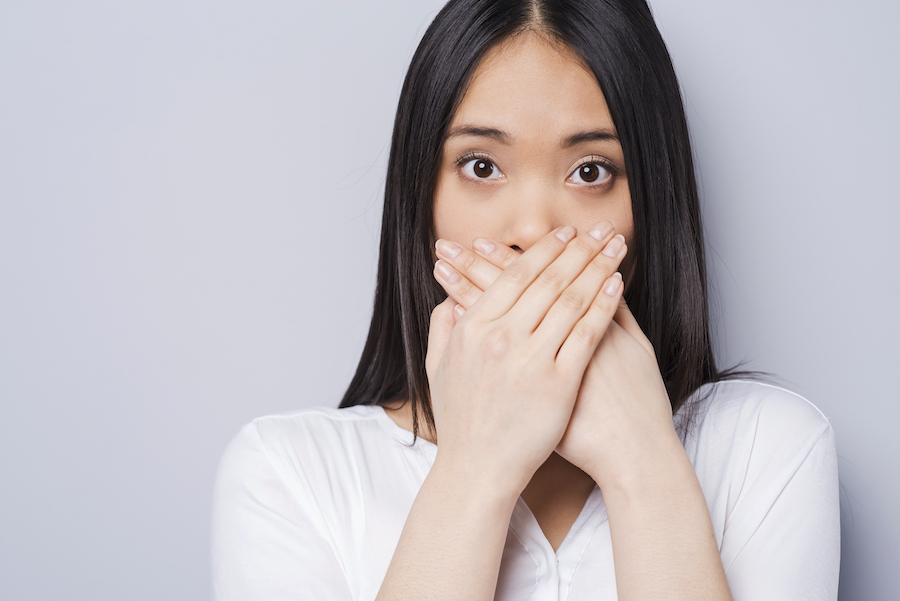 Asian woman covers her mouth in embarrassment due to bad breath