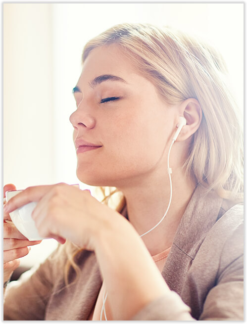woman enjoying a cup of tea while listening to music through her headphones