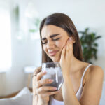 tooth sensitivity, woman wincing from sensitive teeth after drinking ice water