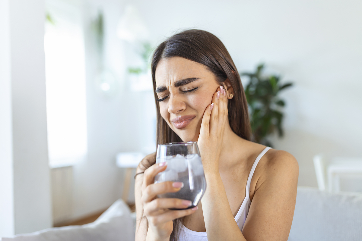tooth sensitivity, woman wincing from sensitive teeth after drinking ice water