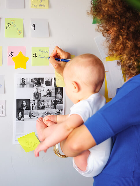 woman holding her baby while writing on a calendar