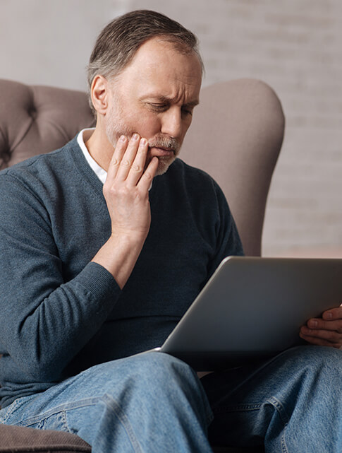 man looking at his laptop while holding his jaw in pain